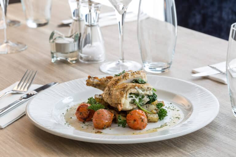 Roast chicken on a bed of potatoes and tomatoes served on a plate